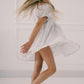 Girl in a white dress standing against a plain background