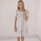 Young girl wearing a white dress with a subtle pattern against a plain background