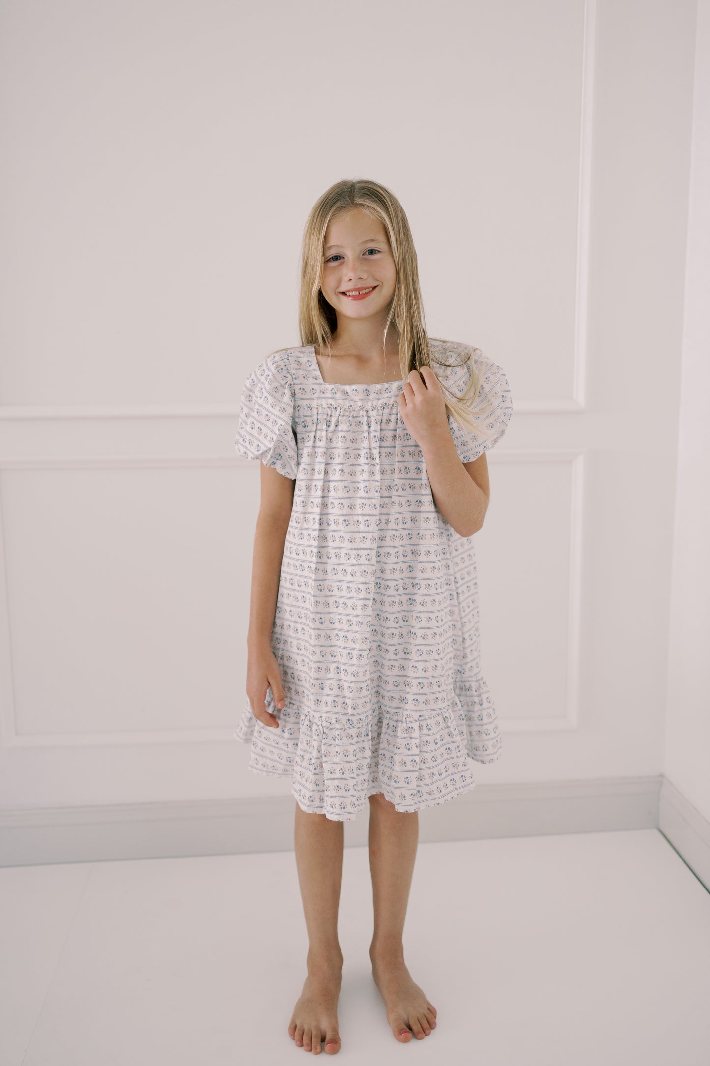 Young girl wearing a white dress with a subtle pattern against a plain background