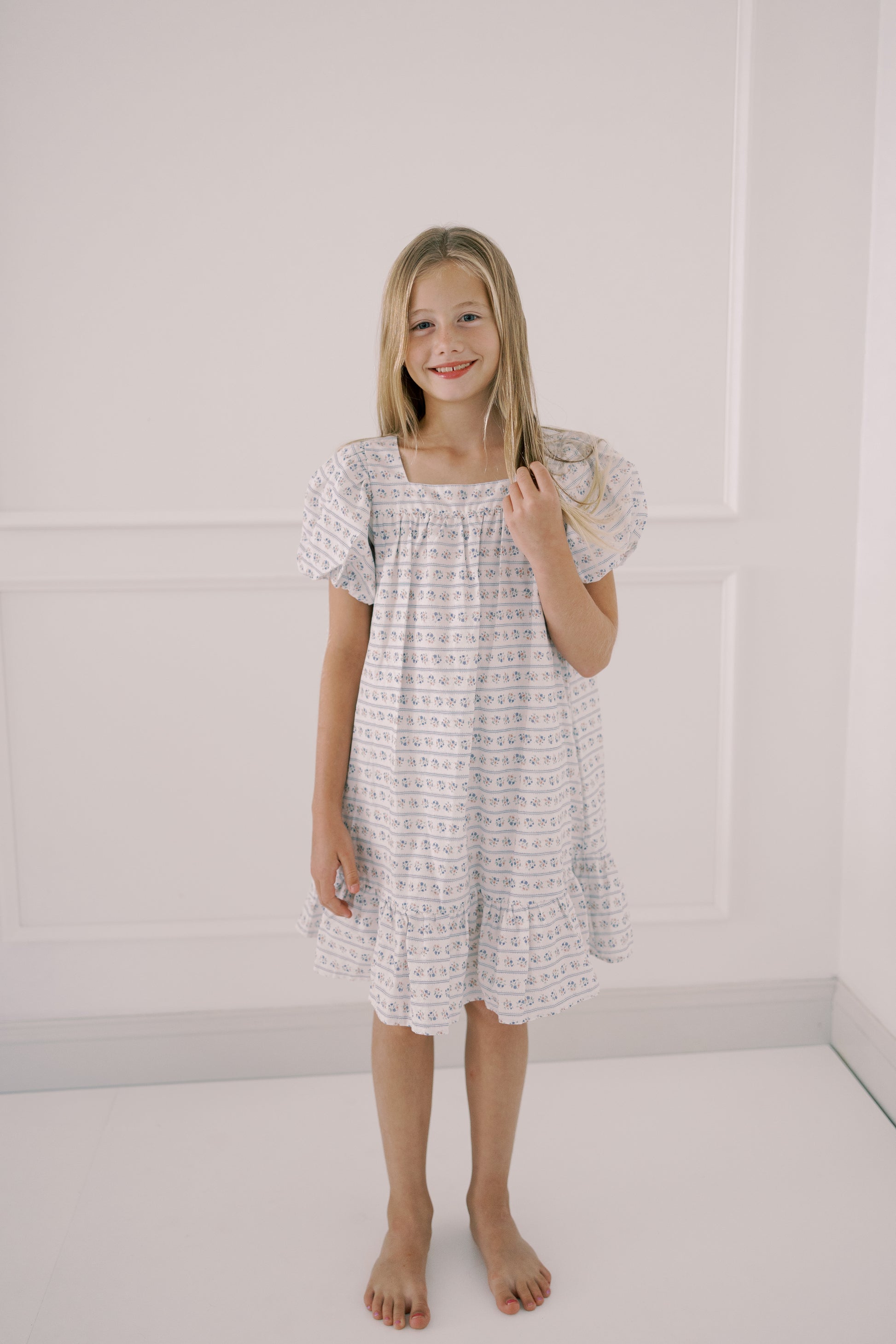 Young girl wearing a white dress with a subtle pattern against a plain background