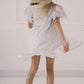 Person wearing a white textured dress against a plain background