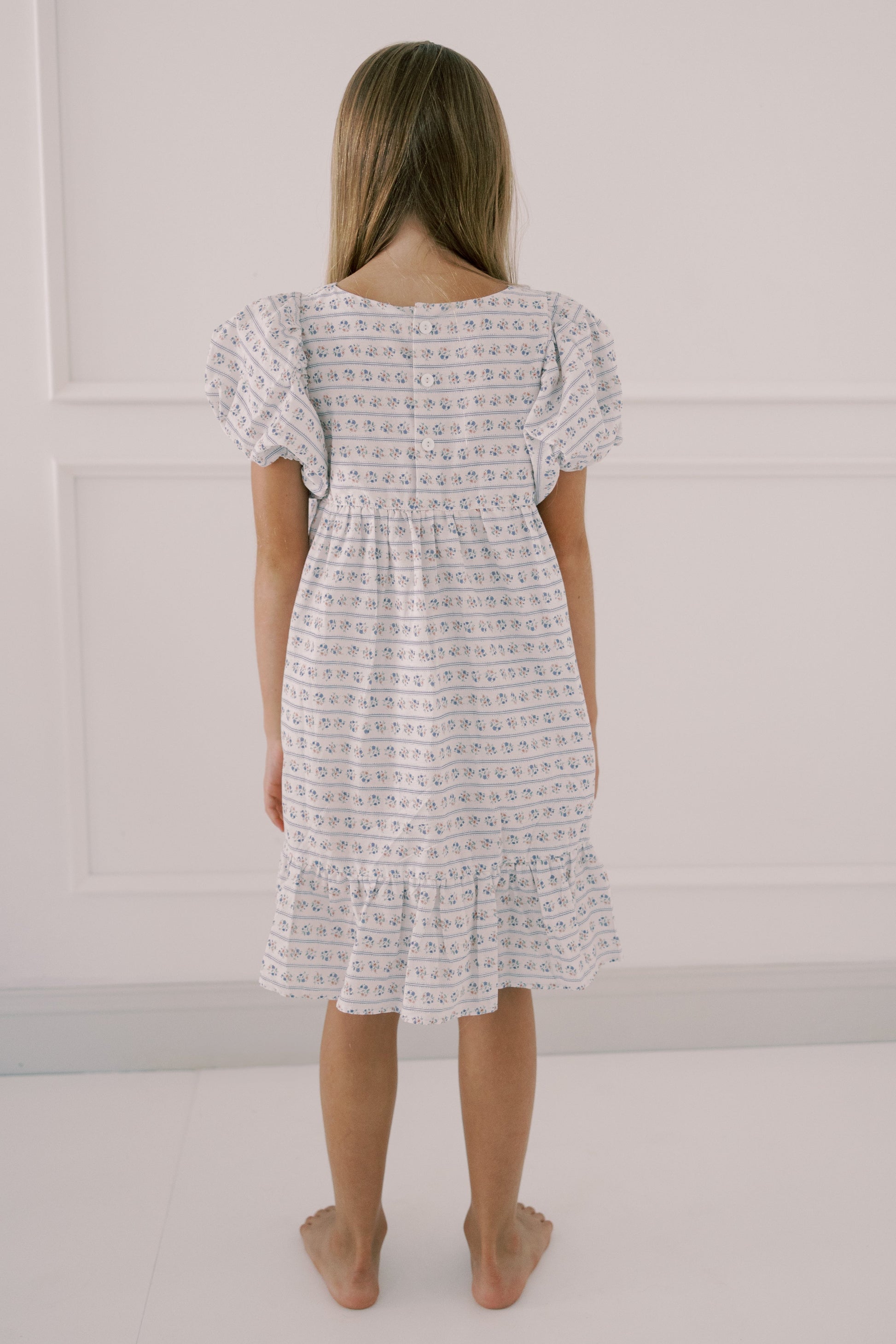 Girl wearing a patterned dress standing against a plain background